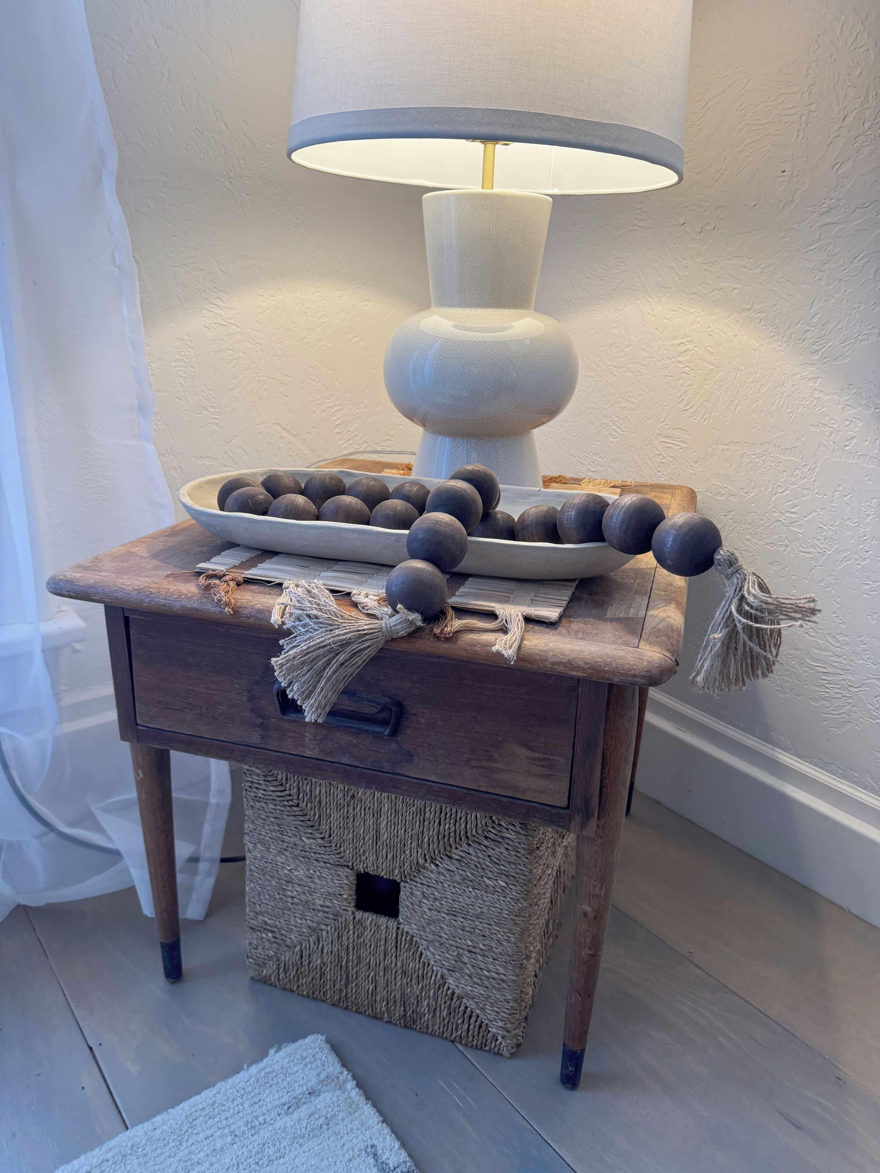 A wooden nightstand with a lamp, a bowl of round objects, and a woven basket.