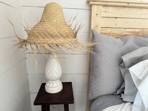 Een kamer met een lamp van geweven riet op een witte voetstuk, een grijs gestreept kussen en een houten hoofdbord.