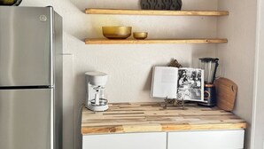Et køkken med træhylder, kaffemaskine, blender og køleskab.