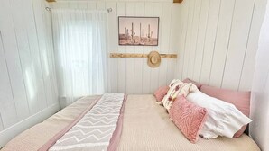 Makuuhuone, jossa on sänky, ikkuna verhoilla, seinälle ripustettu taulu ja puupalkkinen katto.