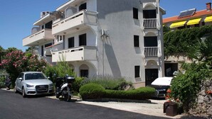 Un edificio residencial de varios pisos con balcones, coches aparcados y abundante vegetación.