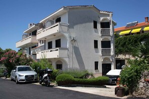A multi-story residential building with balconies, parked cars, and lush greenery. - Holiday apartment with balcony (Krk)