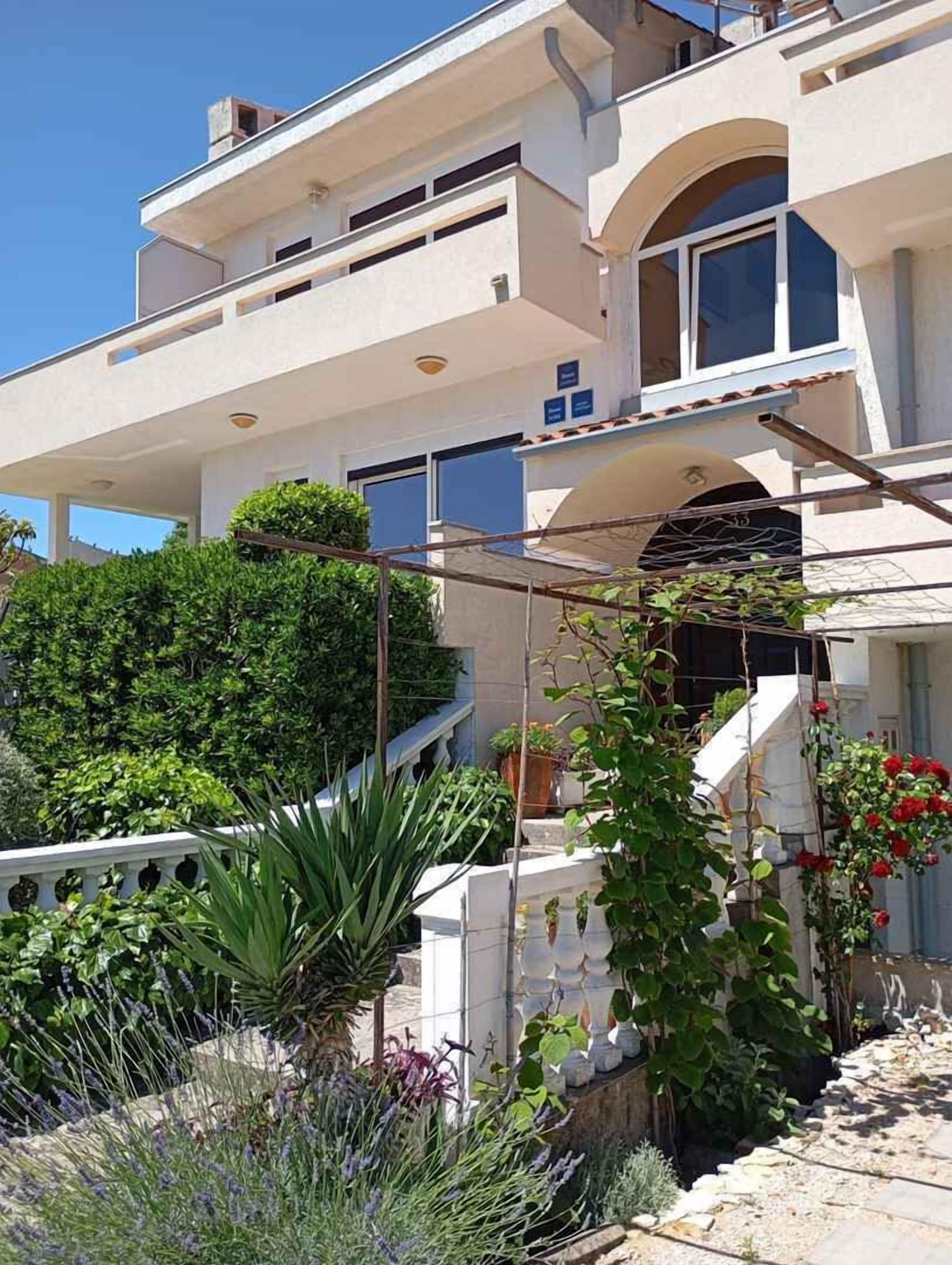 A multi-story building with a balcony, a staircase, and a garden with various plants.