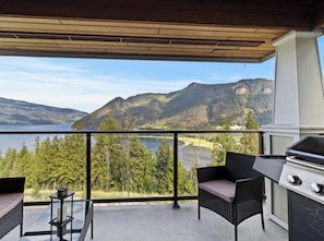 Ein Balkon mit Blick auf einen See und Berge, inklusive Grill, Korbmöbeln und einem kleinen Tisch mit Kerze.