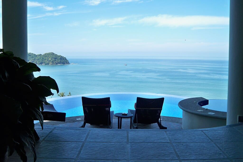 Une vue sur la piscine, avec deux chaises et une table, donnant sur une mer calme et une île lointaine.
