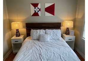 A neatly made bed with white bedding, two bedside tables with lamps, and two wall decorations. - Convenient Wichita Townhome (Wichita)