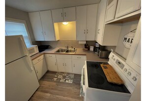 A compact kitchen with white cabinets, a built-in microwave, a stove, and a sink. - Convenient Wichita Townhome (Wichita)