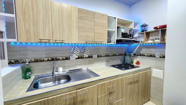 A kitchen with wooden cabinets, a stainless steel sink, and blue under-cabinet lighting.