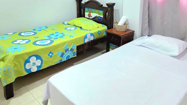 A room with two beds, a ceiling fan, a nightstand, and a curtain.