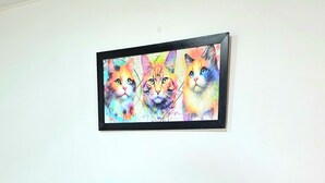 A bed with a colorful floral bedspread, a blue upholstered headboard, and a framed painting of cats above it.