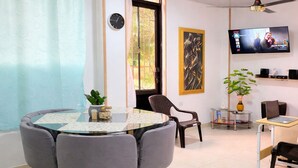 A dining area with a round table, chairs, a clock, a TV, and a plant.
