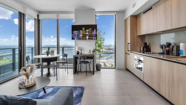 Een moderne keuken met uitzicht over de stad, een eethoek met tafel en stoelen, en een groot raam.