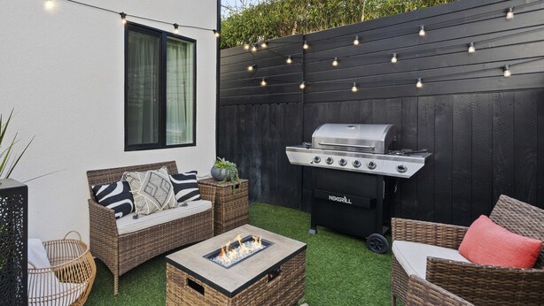 Une terrasse dotée de meubles en osier, d’un barbecue et de guirlandes lumineuses.