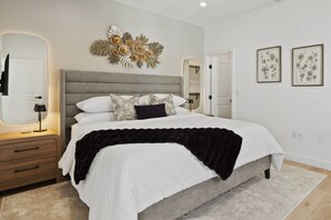 A bedroom with a bed, bedside tables, a mirror, wall art, and a door. - Modern Highland Park Home with 3 Ensuite Bedrooms, Patio & BBQ (Los Angeles)