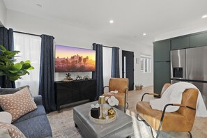 A modern living room with a flat-screen TV, leather sofas, a coffee table, and a kitchen area with a stainless steel refrigerator. - Modern Highland Park Home with 3 Ensuite Bedrooms, Patio & BBQ (Los Angeles)