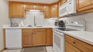 A modern kitchen with wooden cabinets, white countertops, a dishwasher, a stove, and a microwave. - She305 Summit House East 1 Bedroom Condo (Copper Mountain)