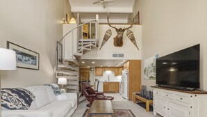 A modern living room with a sofa, a red leather chair, a coffee table, a TV, and a staircase leading to an upper level. - She305 Summit House East 1 Bedroom Condo (Copper Mountain)