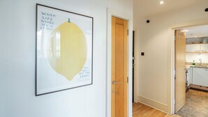 A hallway with a framed artwork, a wooden door, and a glimpse of a kitchen area. - Bright 1BR in Central Clerkenwell (London)
