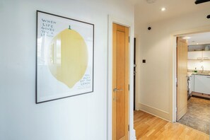 A hallway with a framed artwork, a wooden door, and a glimpse of a kitchen area. - Bright 1BR in Central Clerkenwell (London)