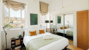 A hotel room with a bed, bedside lamps, a desk, a chair, a wardrobe, and a window with curtains. - Bright 1BR in Central Clerkenwell (London)