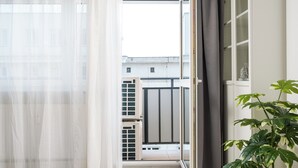 Ein Zimmer mit einer Schiebeglastür, die auf einen Balkon führt, einer Zimmerpflanze und einem Fenster mit durchscheinenden Vorhängen.