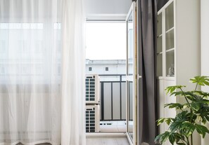 A room with a sliding glass door leading to a balcony, a potted plant, and a window with sheer curtains. - Chmielna Downtown Homely Apartment (Warszawa)