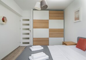 A modern bedroom with a bed, a nightstand, a wooden wardrobe, and a wall-mounted shelf. - Chmielna Downtown Homely Apartment (Warszawa)