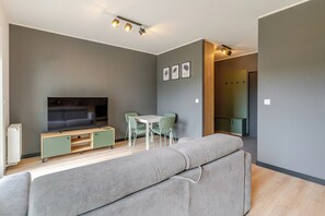 Ein modernes Wohnzimmer mit einem Flachbildfernseher, einer Couch, einem Esstisch mit Stühlen und einer Holzkommode.