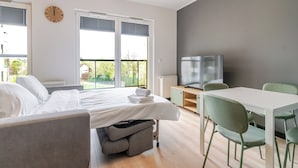 A modern hotel room with a bed, a TV, a dining table, and green chairs. - Sowińskiego Modern Studio (Gliwice)
