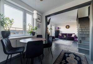 Una sala de estar moderna con comedor, ventanas amplias, una escalera y un sofá morado.