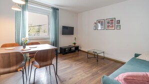 Moderni olohuone, jossa on ruokailutila, puulattia, sohva, televisio ja seinällä tauluja.