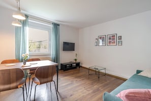 A modern living room with a dining area, wooden flooring, a sofa, a TV, and framed artwork on the wall. - Mastalerza Spacious Apartment (Gliwice)