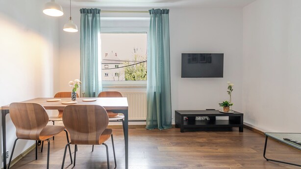 Moderni huone, jossa on ruokapöytä, tuoleja, televisio ja ikkuna, jossa on verhot.