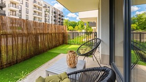 A balcony with a view of a residential building, a woven basket on a table, and a chair with cushions. - Rakowicka Charming Apartment with Garden (Kraków)
