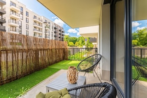 Ein Balkon mit Blick auf ein Wohnhaus, ein gewebter Korb auf einem Tisch und ein Stuhl mit Kissen.