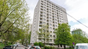 Ein mehrgeschossiges Wohngebäude mit Balkonen, parkenden Autos und Bäumen entlang der Straße.