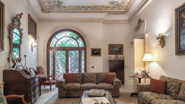 Amplia sala de estar con un ventanal arqueado, techo ornamentado y muebles clásicos.