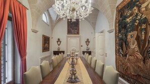 Una larga mesa de comedor con sillas, una araña y un cuadro grande en la pared.