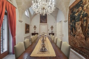 Un lungo tavolo da pranzo con sedie, un lampadario e un grande quadro appeso al muro.