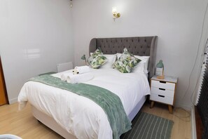 Una cama bien hecha con un cubrecolcha verde, una lámpara de noche y una mesita de noche con cajones.