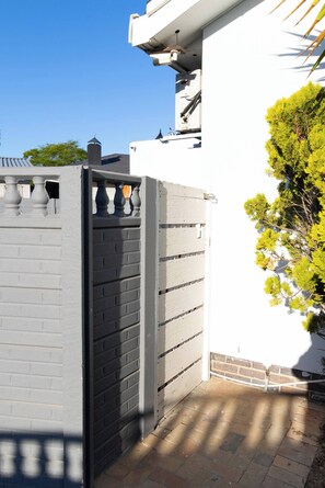 Un área cerrada con un muro blanco, un muro de ladrillo y una puerta metálica.