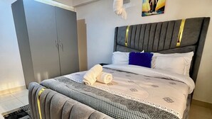 A neatly made bed with a grey headboard, a grey wardrobe, and a painting on the wall.