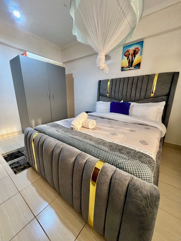 A neatly made bed with a grey headboard, a grey wardrobe, and a painting on the wall.