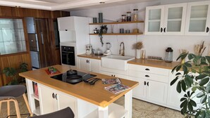 Une cuisine avec des meubles blancs, un plan de travail en bois, un évier, une cuisinière et un coin repas avec des chaises.