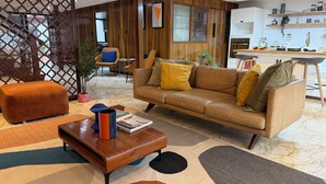 Un salon moderne avec un canapé, un pouf, une table basse et, au fond, un coin cuisine.