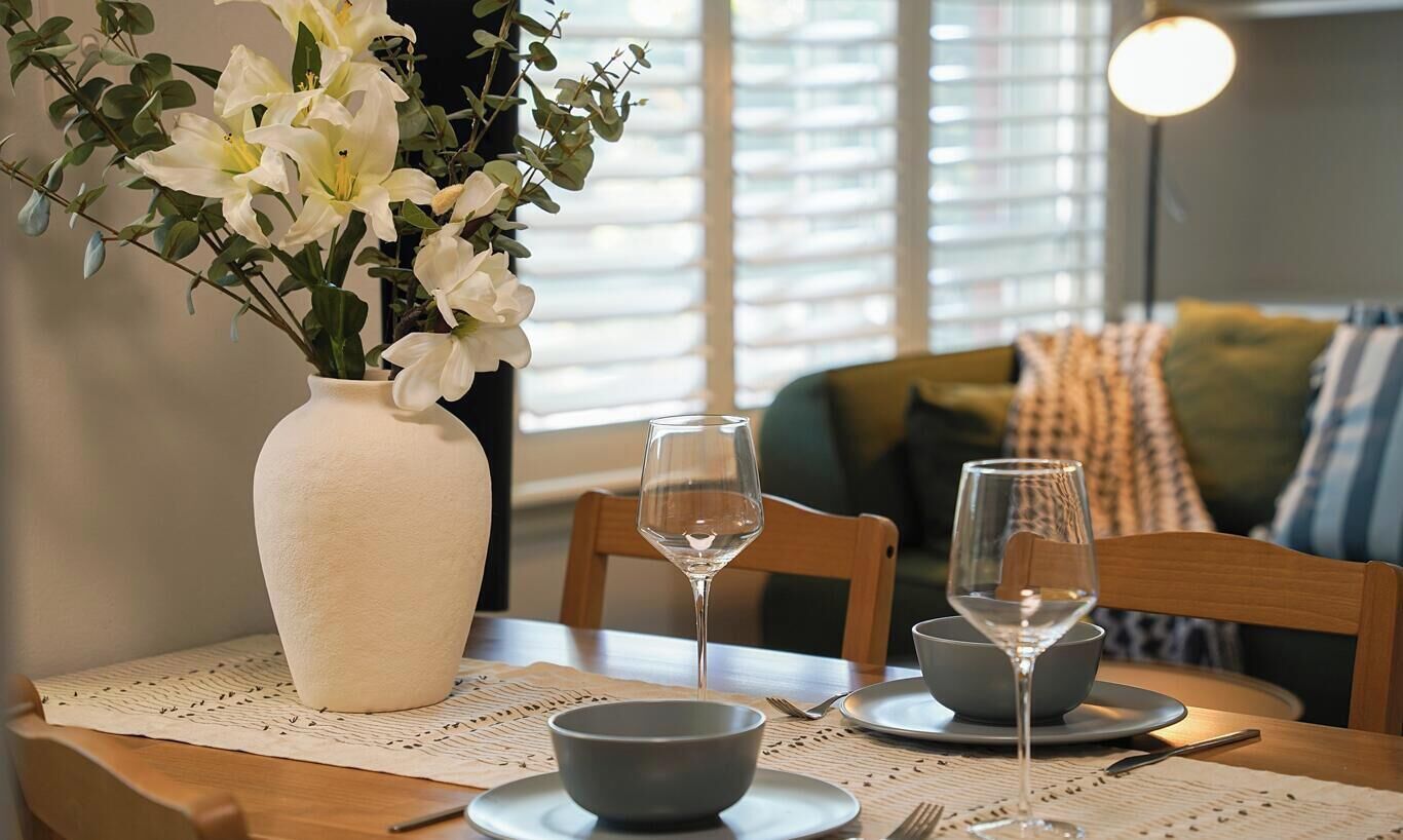 Een eettafel met een bloemenvaas, twee wijnglazen en een schaal.