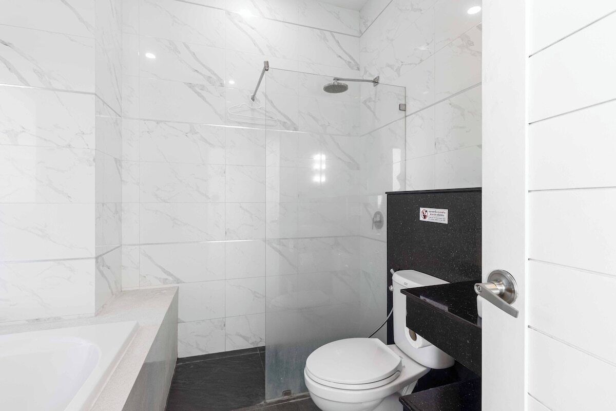 Et moderne badeværelse med en glasvæg omkring brusenichen, et hvidt toilet og et badekar.