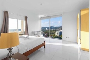 A modern hotel room with a large bed, a desk, a chair, and a view of the city. - Stunning Sea-View Penthouse w/ Pool C80 (Tambon Karon)