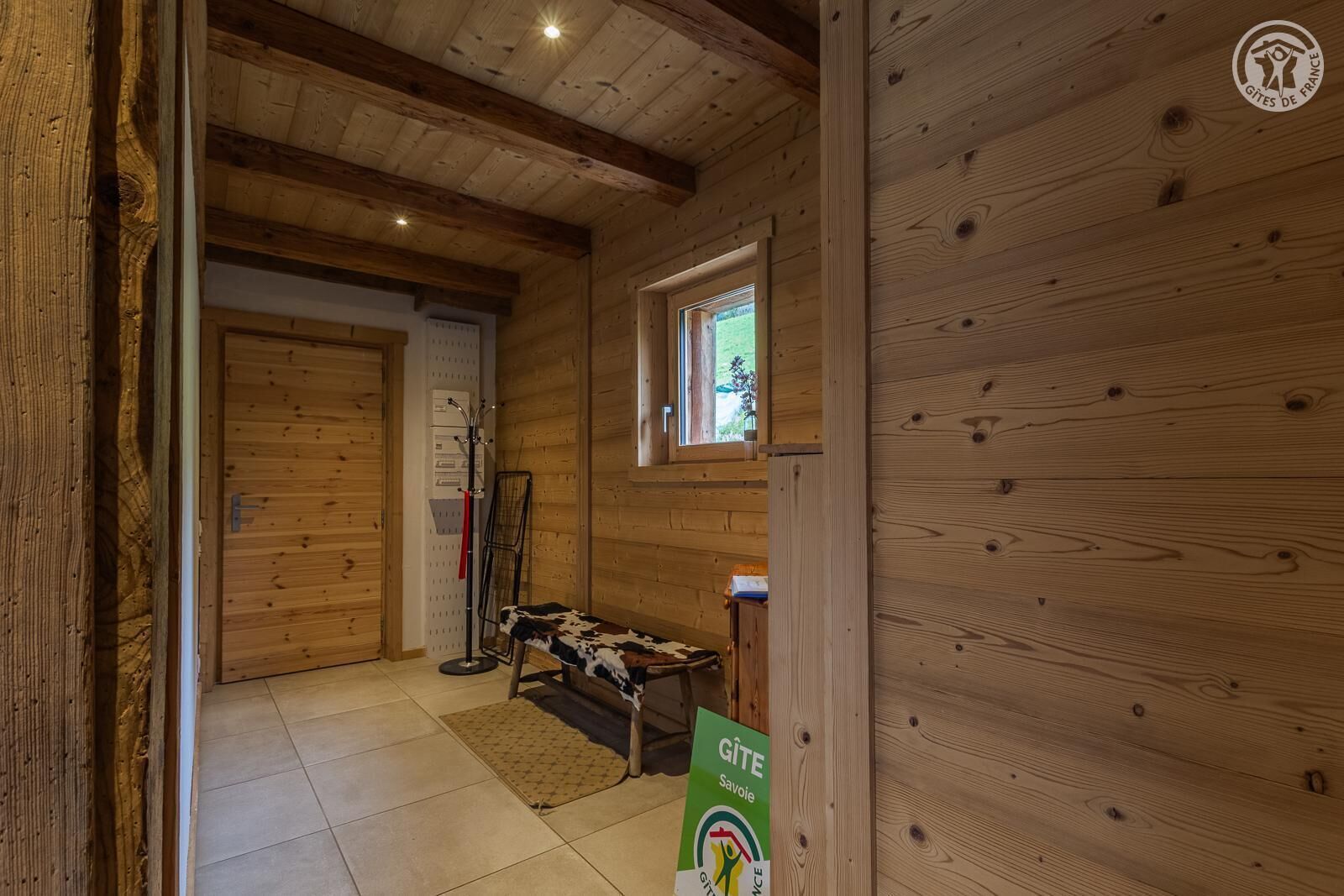 A wooden interior with a bed, a coat rack, and a window.