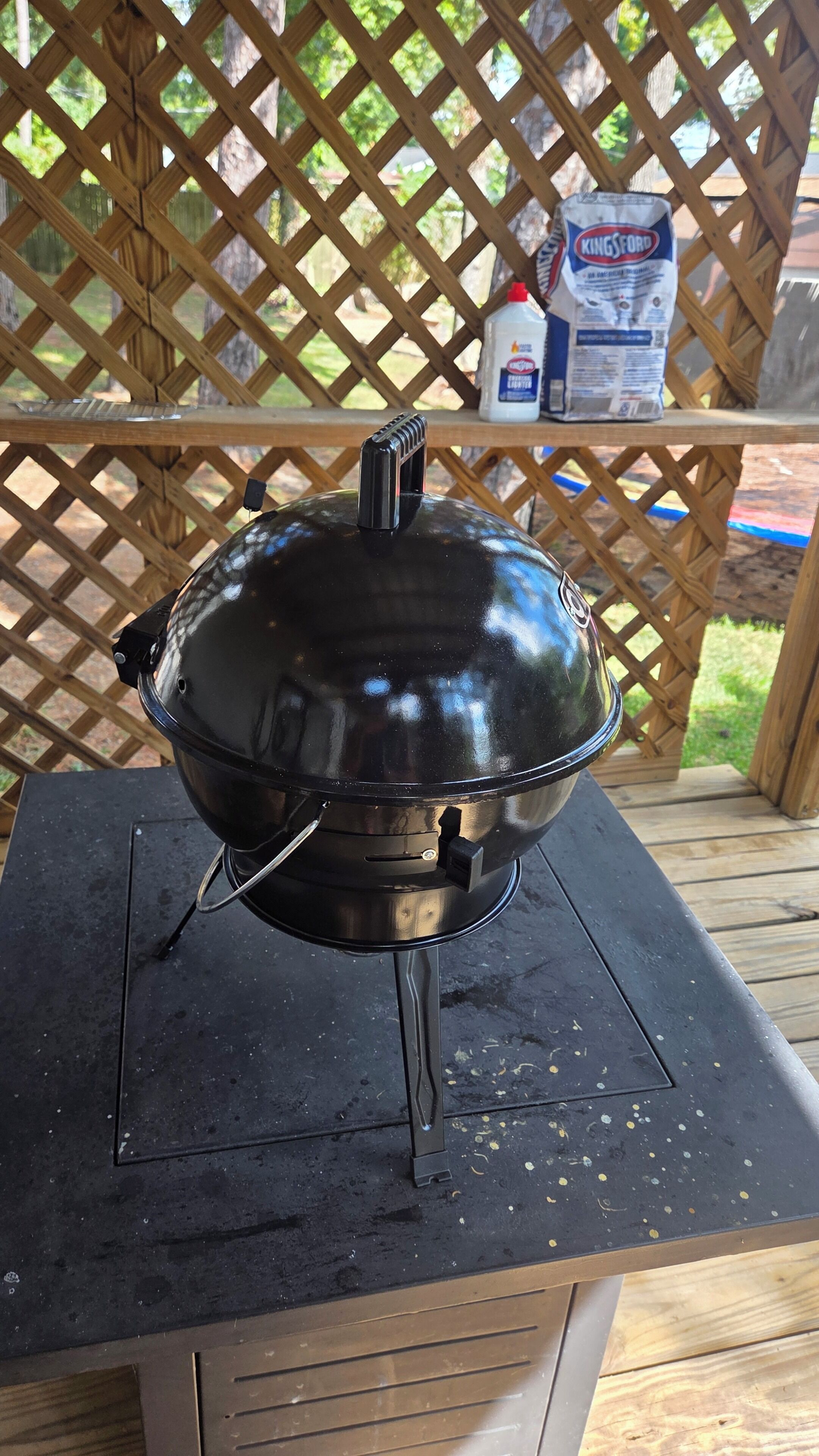 A stainless steel barbecue grill on a black countertop with a wooden lattice fence in the background.
